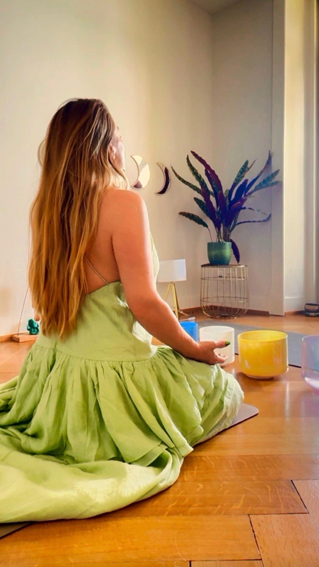 Sandra seated in a green dress before the moon phase mirrors with crystal singing bowls